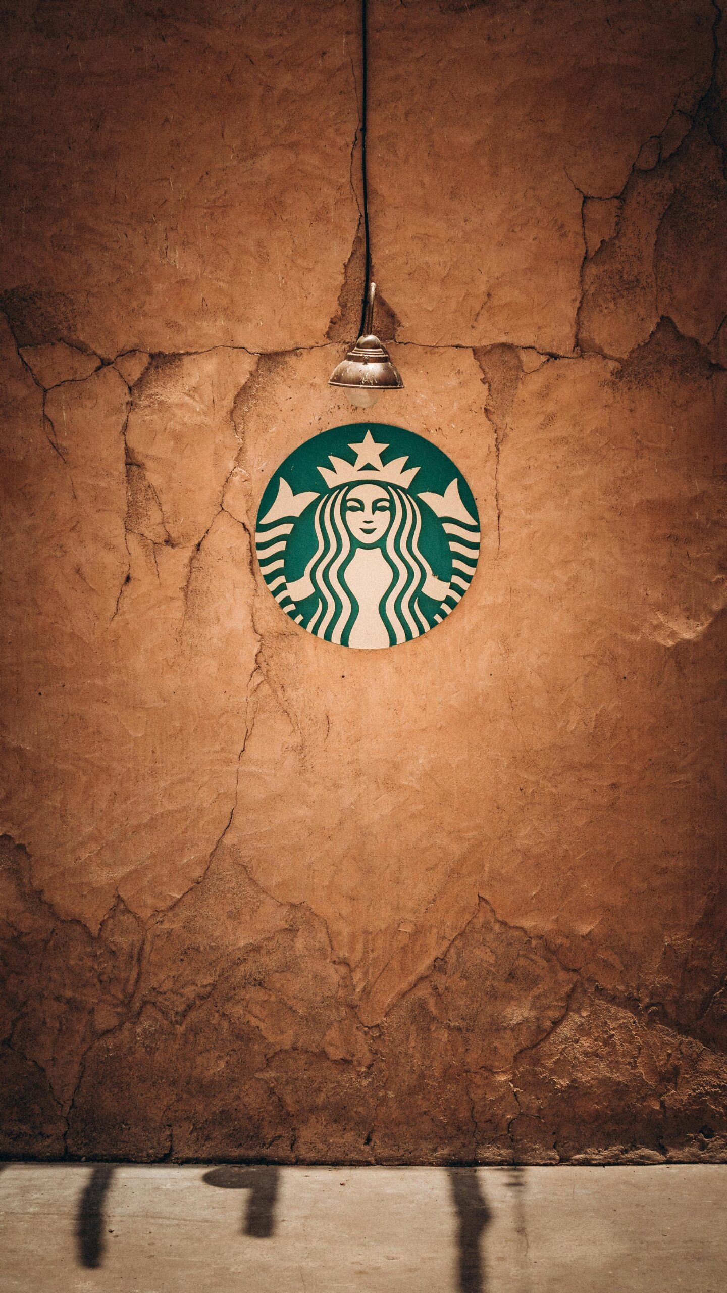 Artistic shot of Starbucks logo on a crackled wall with a vintage lamp, illustrating texture and atmosphere.